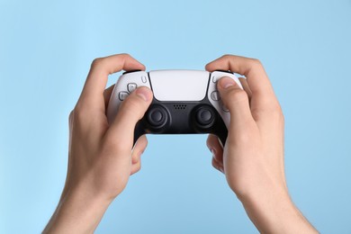 Man using wireless game controller on light blue background, closeup