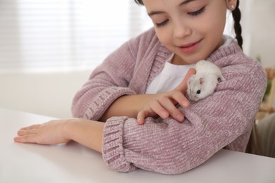 Photo of Little girl with cute hamster at table indoors
