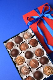 Photo of Box with delicious chocolate candies on blue background, above view