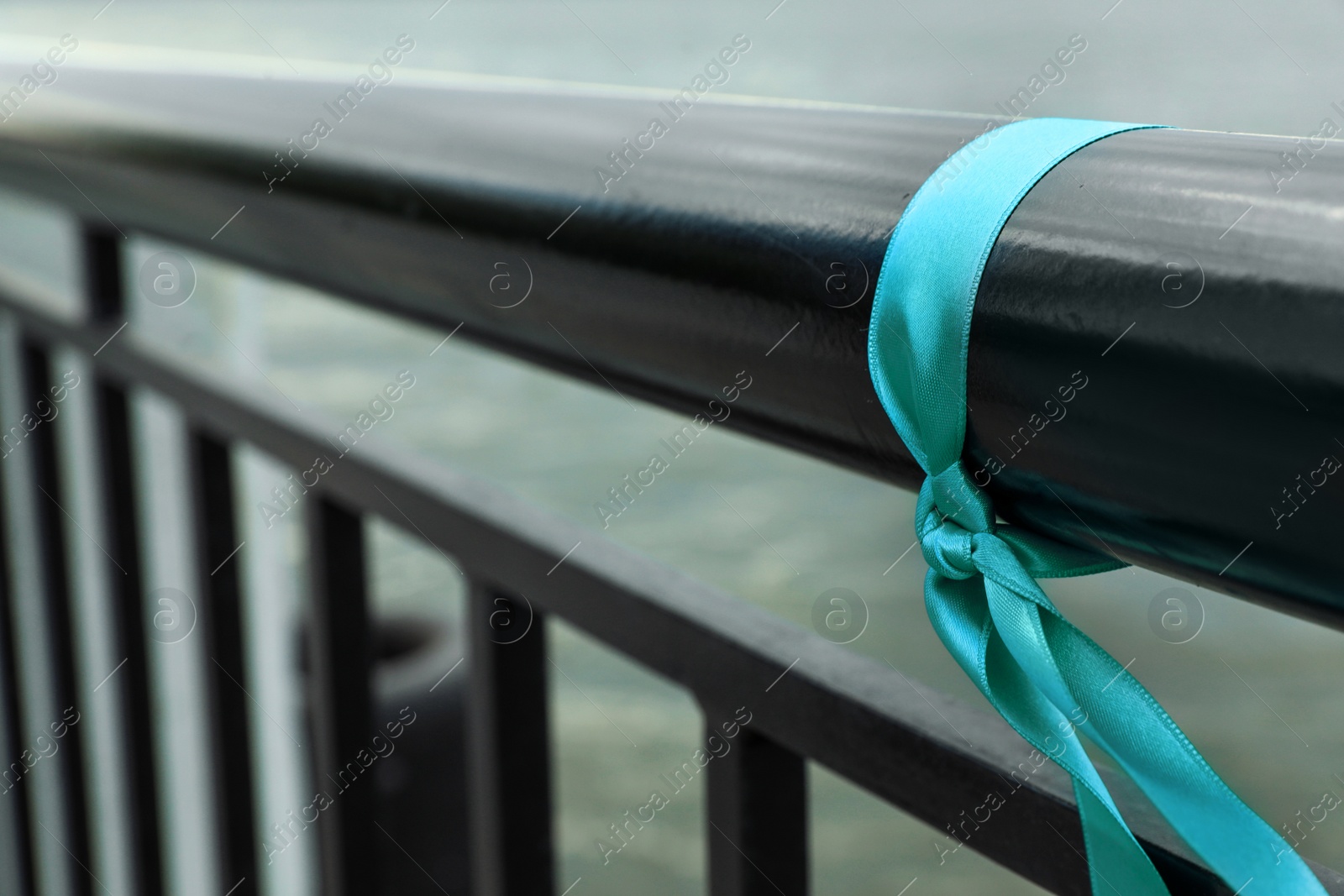 Photo of Teal ribbon tied to railing outdoors, space for text