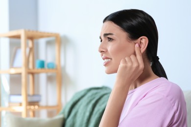 Young woman suffering from ear pain at home