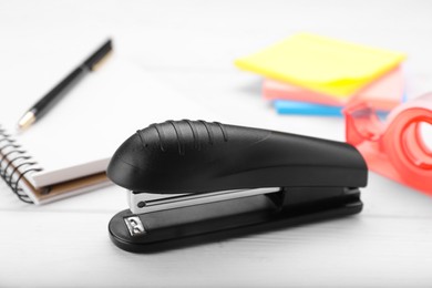 Photo of New bright stapler with stationery on white wooden table, closeup