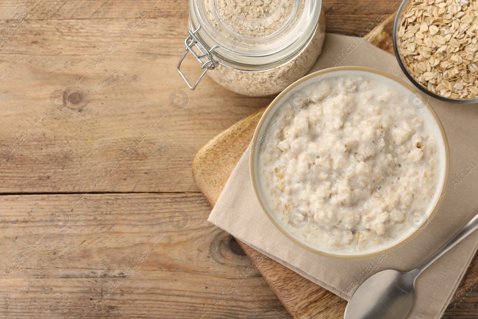 Photo of Tasty boiled oatmeal in bowl, flakes and spoon on wooden table, flat lay. Space for text