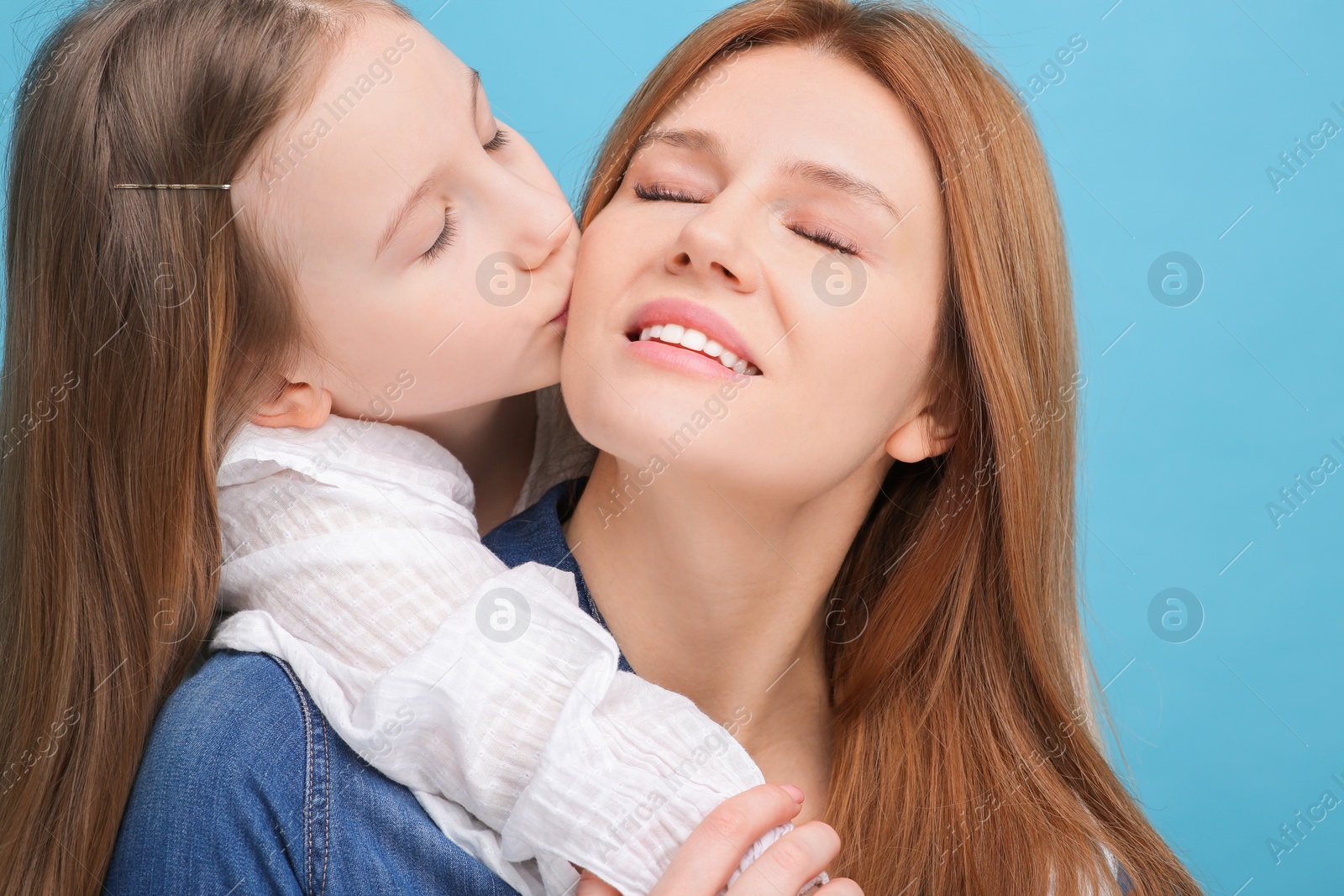 Photo of Portrait of happy mother and her cute daughter on light blue background, closeup