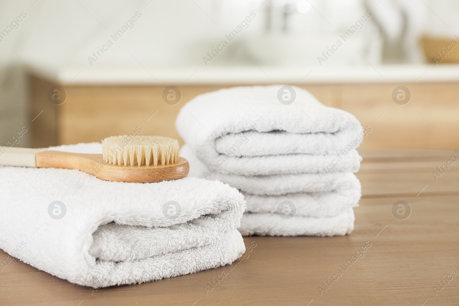 Photo of Stack of clean towels and massage brush on wooden table in bathroom