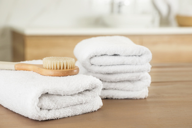 Photo of Stack of clean towels and massage brush on wooden table in bathroom