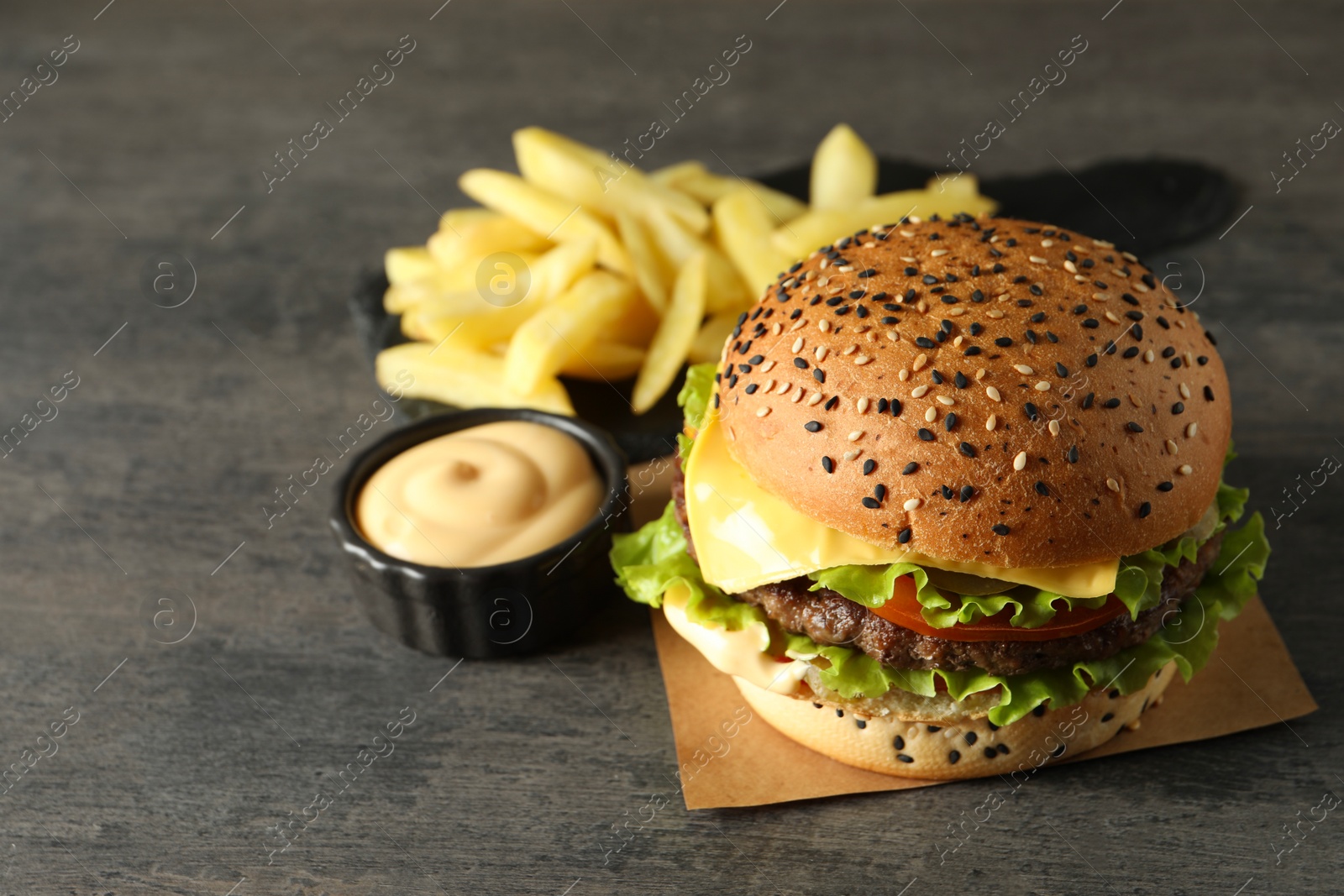 Burger with delicious patty, french fries and sauce on gray table Photo of Burger with delicious patty, french fries and sauce on gray table