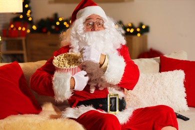 Photo of Merry Christmas. Emotional Santa Claus with popcorn bucket watching TV on sofa at home