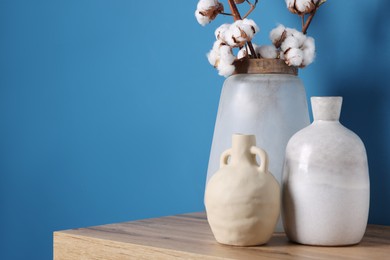 Photo of Vases and cotton branches on wooden table indoors. Space for text