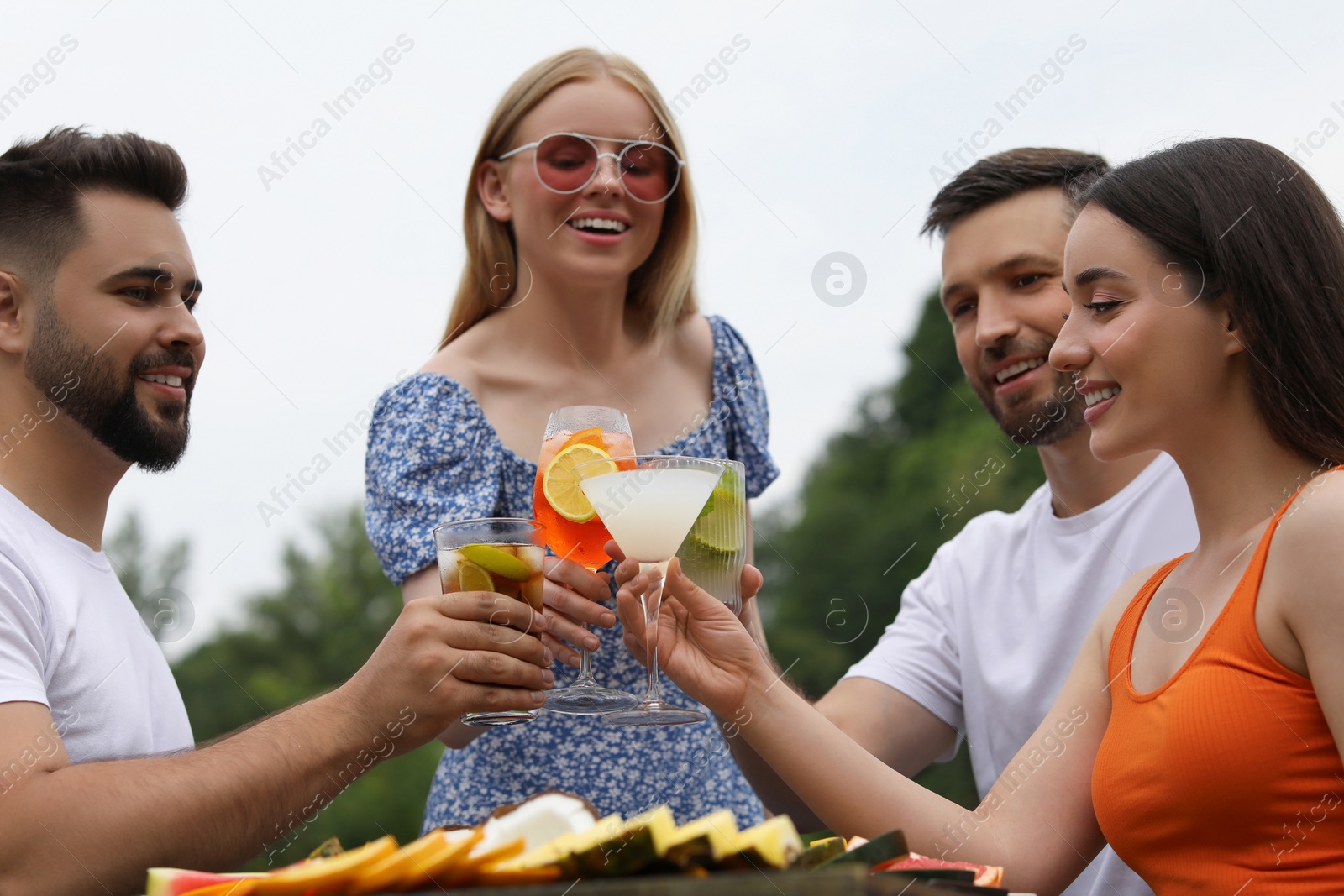 Photo of Happy friends clinking glasses with cocktails at table outdoors