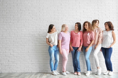 Group of women with silk ribbons near brick wall, space for text. Breast cancer awareness concept