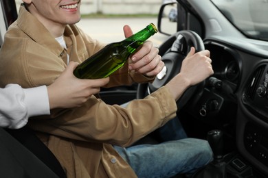 Smiling man taking bottle of beer while driving car, closeup. Don't drink and drive concept