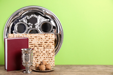 Photo of Symbolic Pesach (Passover Seder) items on wooden table against green background, space for text