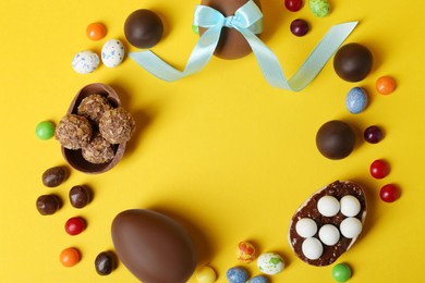 Frame of chocolate eggs and candies on yellow background, flat lay. Space for text