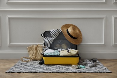 Photo of Open suitcase with summer clothes, accessories and shoes near white wall indoors