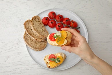 Photo of Woman eating delicious tomato bruschetta at white wooden table, top view