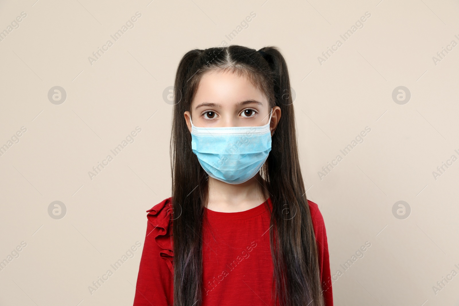 Photo of Little girl in medical mask on beige background. Virus protection
