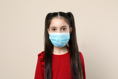 Photo of Little girl in medical mask on beige background. Virus protection