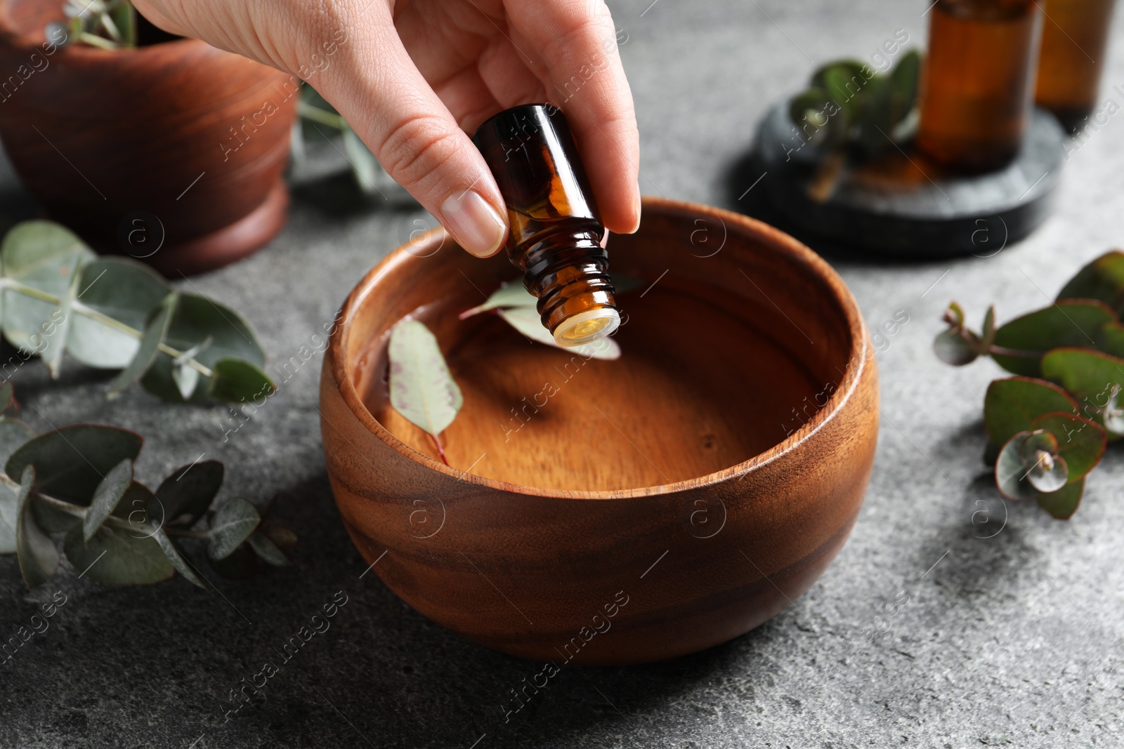 Photo of Woman dripping eucalyptus essential oil from bottle into bowl at light grey table, closeup