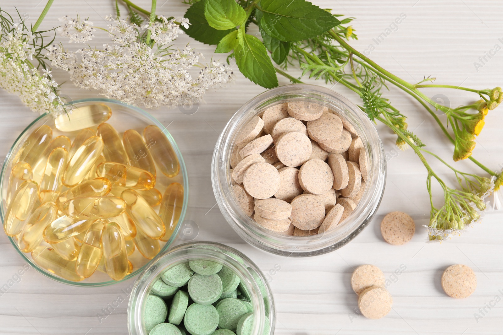 Photo of Different pills, flowers and herbs on white wooden table, flat lay. Dietary supplements