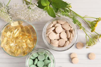 Different pills, flowers and herbs on white wooden table, flat lay. Dietary supplements