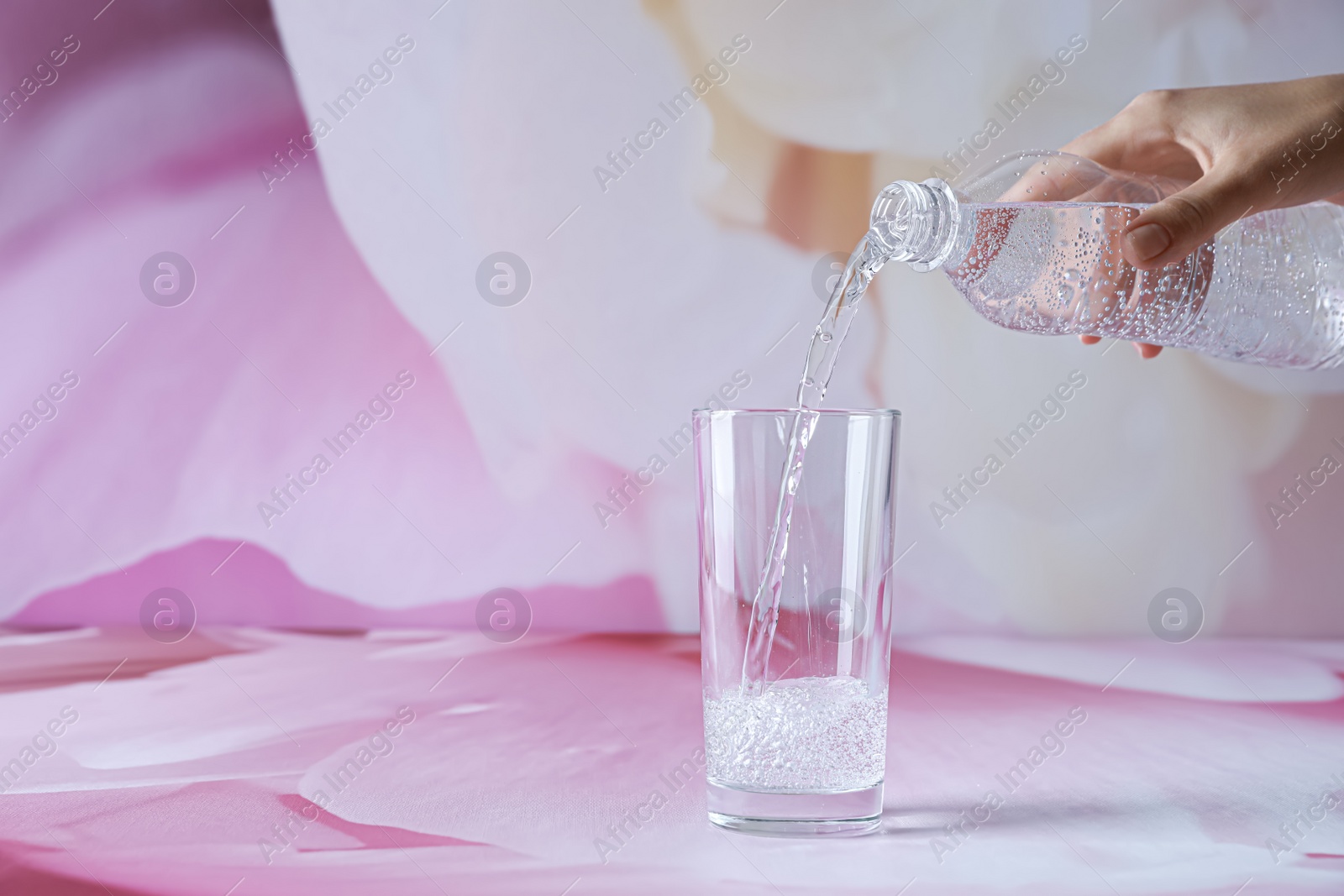 Photo of Woman pouring water from bottle into glass on color background, closeup. Space for text