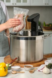 Photo of Woman putting vacuum packed meat into pot in kitchen, closeup. Thermal immersion circulator for sous vide cooking