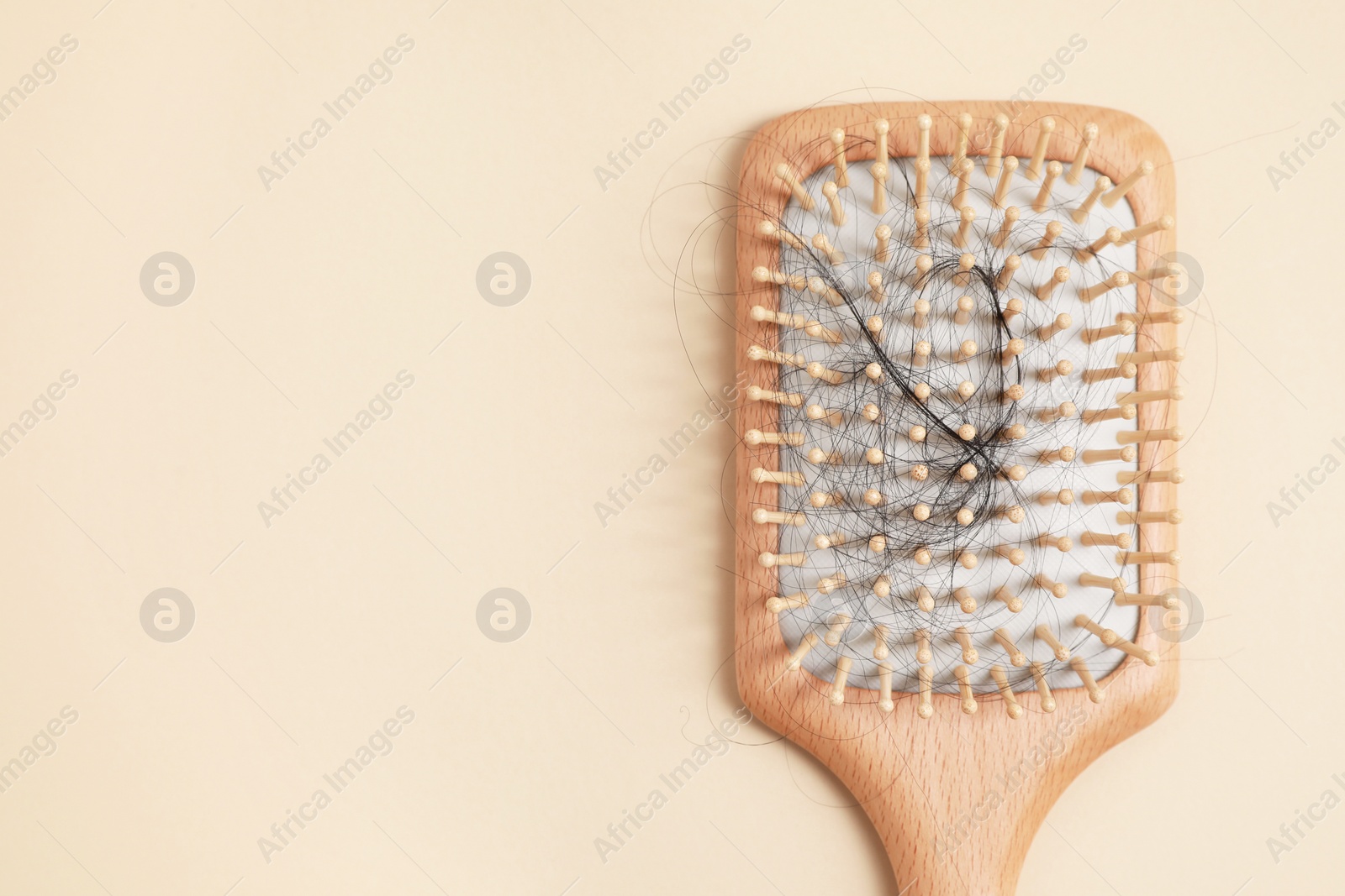 Photo of Wooden brush with lost hair on beige background, top view. Space for text