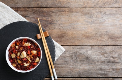 Photo of Slate plate with bowl of cooked brown rice and chopsticks on table, top view. Space for text