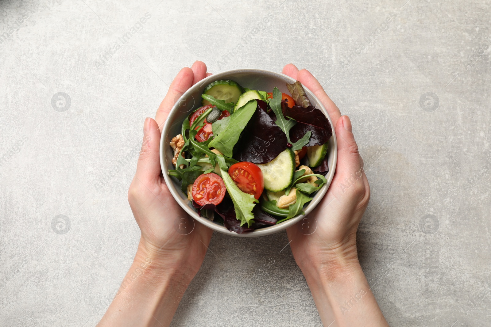 Photo of Woman with tasty fresh vegetarian salad at grey table, top view