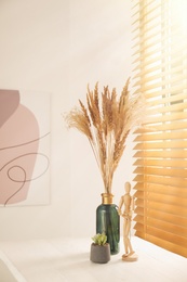 Photo of Dry plants on white wooden table near window indoors. Interior design