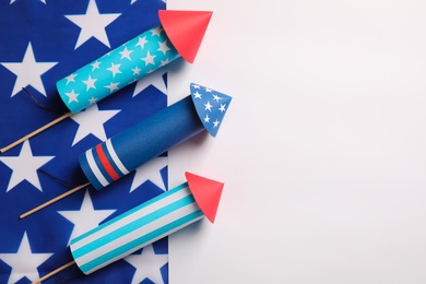 Photo of Firework rockets and USA flag on white background, flat lay with space for text. Festive decor