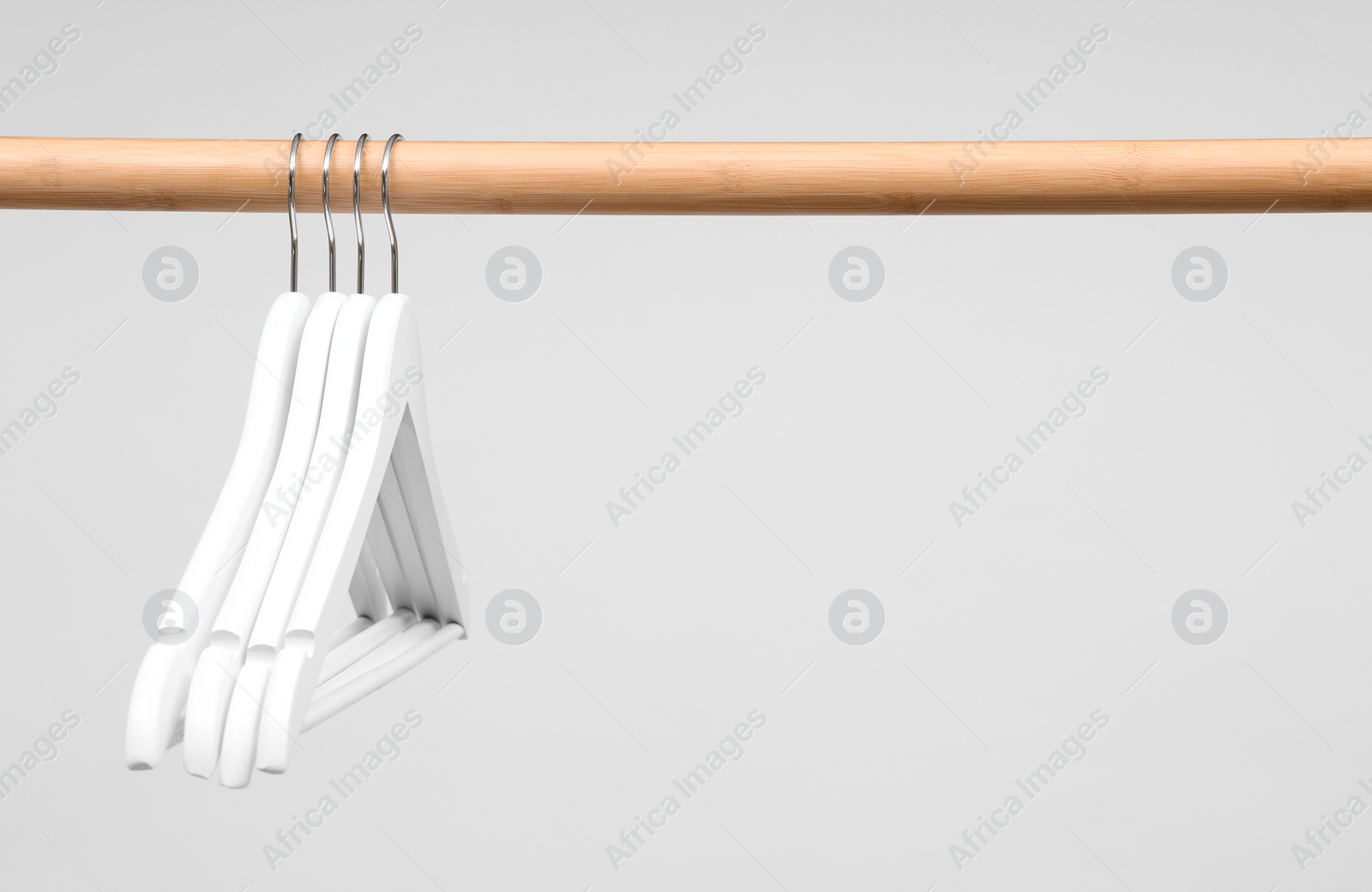 Photo of Empty clothes hangers on wooden rail against light background. Space for text