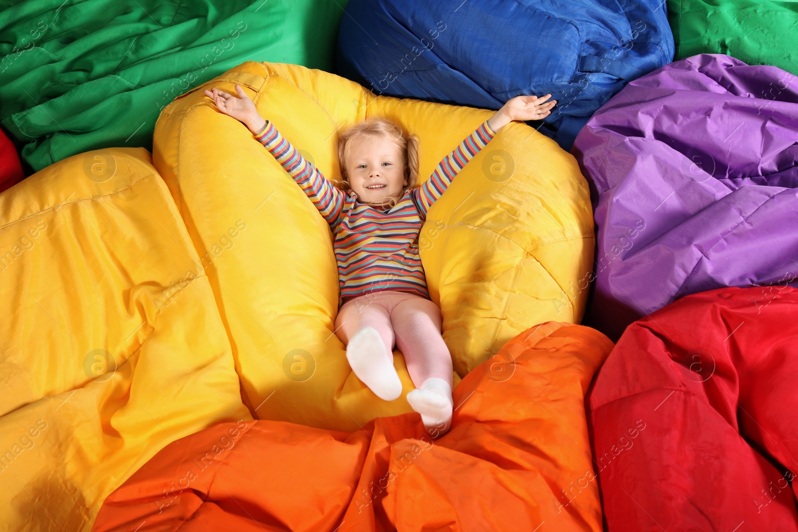 Photo of Cute child playing on colorful bean bag chairs indoors