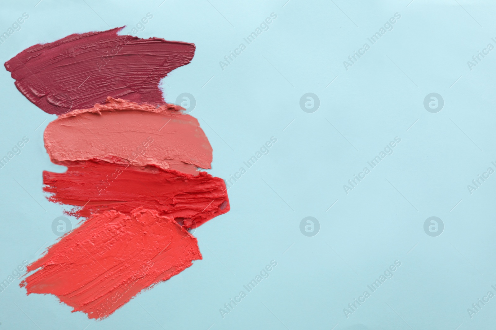 Photo of Smears of different beautiful lipsticks on light blue background, top view. Space for text