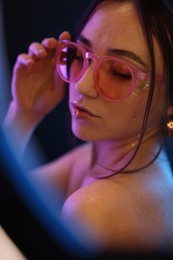 Photo of Beautiful woman in glasses on dark background in neon lights, view through ring lamp