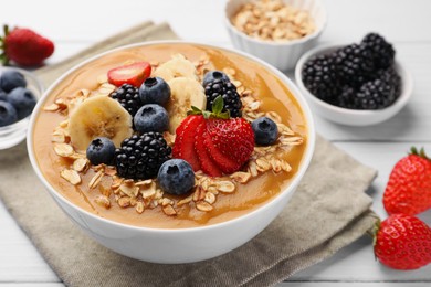 Photo of Delicious smoothie bowl with fresh berries, banana and oatmeal on white wooden table, closeup