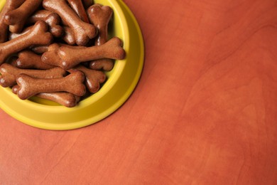 Yellow bowl with bone shaped dog cookies on wooden table, above view. Space for text