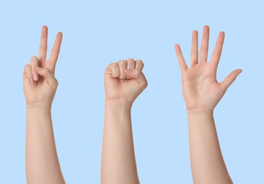 People playing rock, paper and scissors on light blue background, closeup