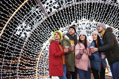 Happy friends with cups of mulled wine at winter fair. Space for text