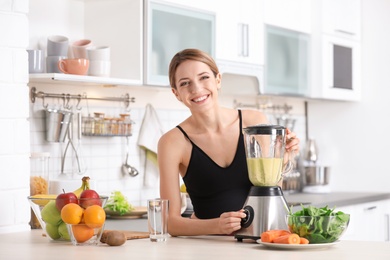 Photo of Young woman preparing tasty healthy smoothie at table in kitchen