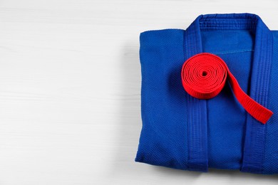 Red karate belt and blue kimono on wooden background, top view. Space for text