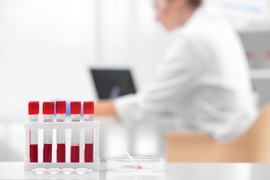 Test tubes with blood samples and scientist working on computer in laboratory