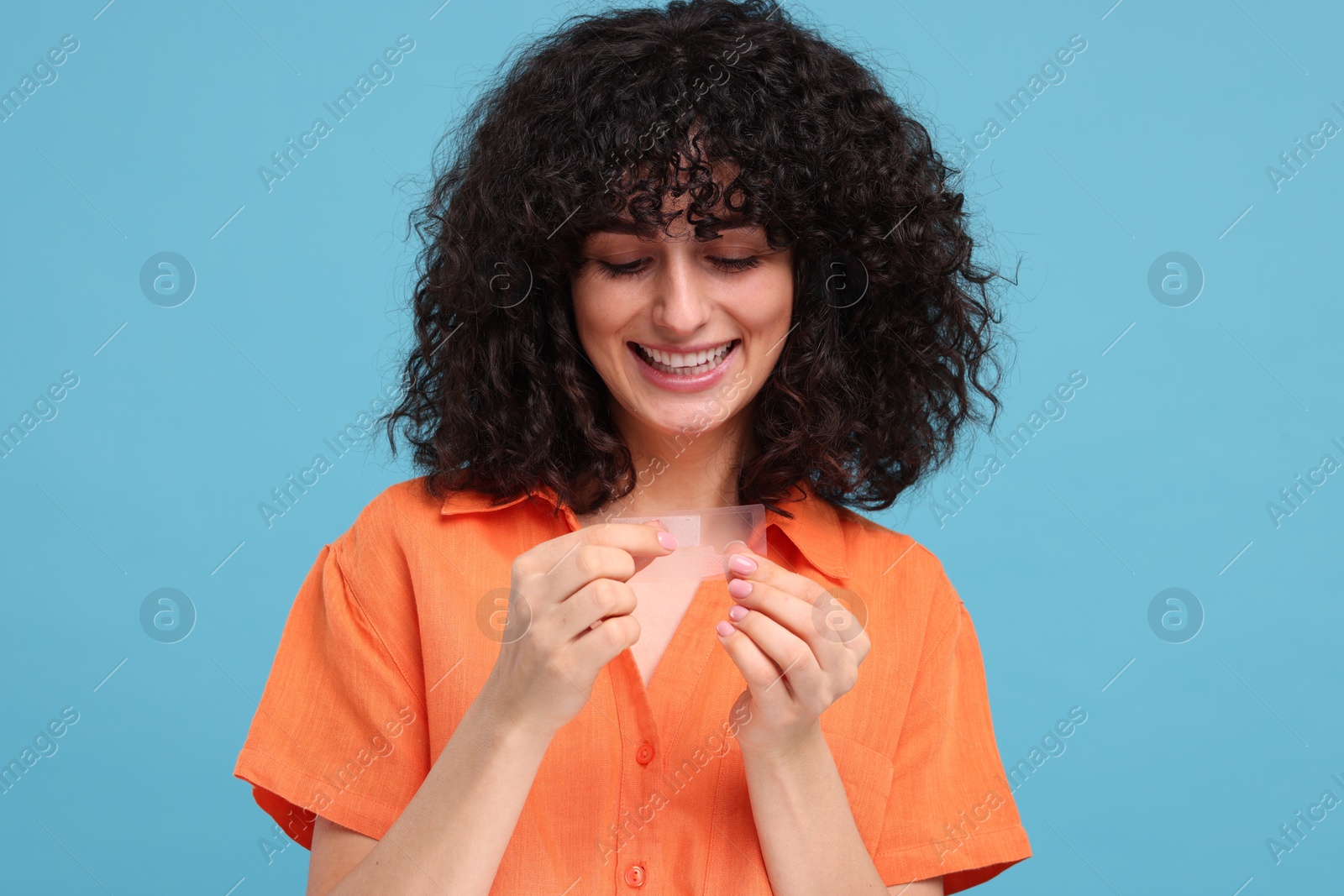 Photo of Young woman holding teeth whitening strips on light blue background