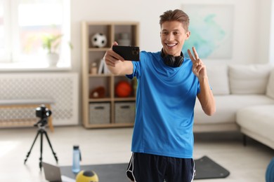 Smiling sports blogger streaming online fitness lesson with smartphone at home