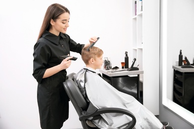 Professional female hairdresser working with little boy in salon