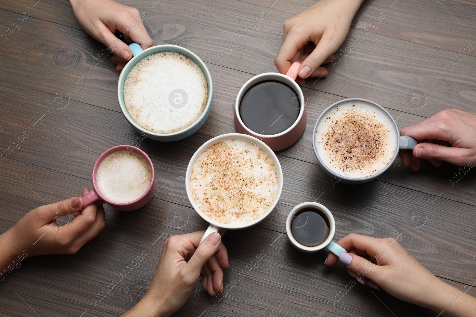 Photo of People holding different cups with aromatic hot coffee at wooden table, top view