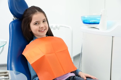 Photo of Cute little girl in chair at dentist's office. Space for text