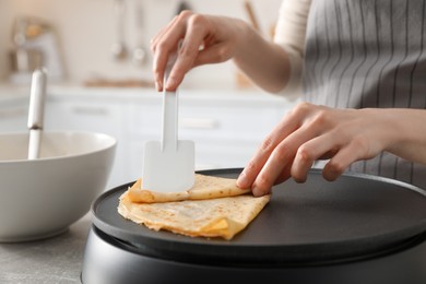 Woman cooking delicious crepe on electric pancake maker in kitchen, closeup