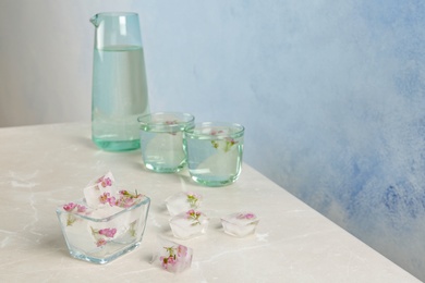 Photo of Bowl with floral ice cubes on table against color background. Space for text